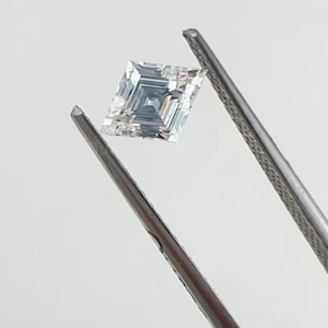 Könnte beinhalten: Ein quadratisch geschliffener, im Labor hergestellter Diamant, der von einer Pinzette gehalten wird. Der Diamant ist ein klarer, funkelnder Stein mit einem Lozen-Schliff. Der Text über dem Diamanten lautet "0.56 CT Lozen Cut Lab Diamond".