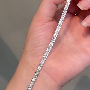 Pu&ograve; includere: Un bracciale tennis color argento caratterizzato da una fila continua di piccole pietre trasparenti a taglio rettangolare incastonate in una montatura metallica. Il bracciale ha un design lineare e sottile con finitura lucida e chiusura.