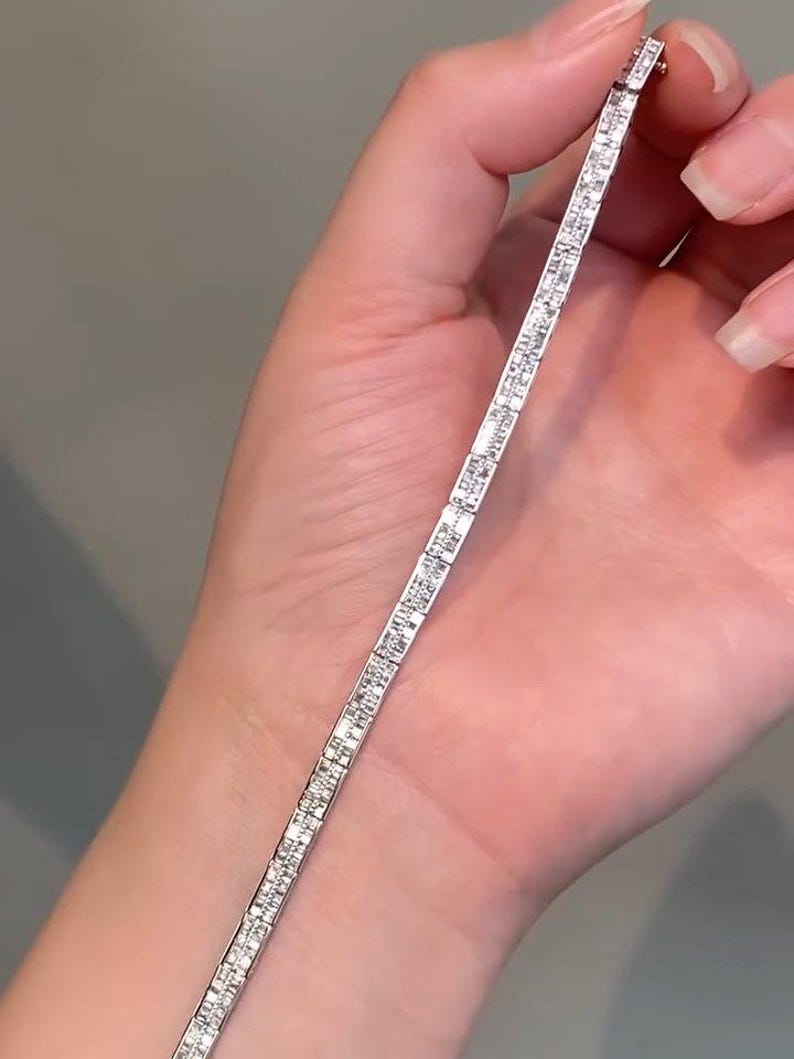 Pu&ograve; includere: Un bracciale tennis color argento caratterizzato da una fila continua di piccole pietre trasparenti a taglio rettangolare incastonate in una montatura metallica. Il bracciale ha un design lineare e sottile con finitura lucida e chiusura.