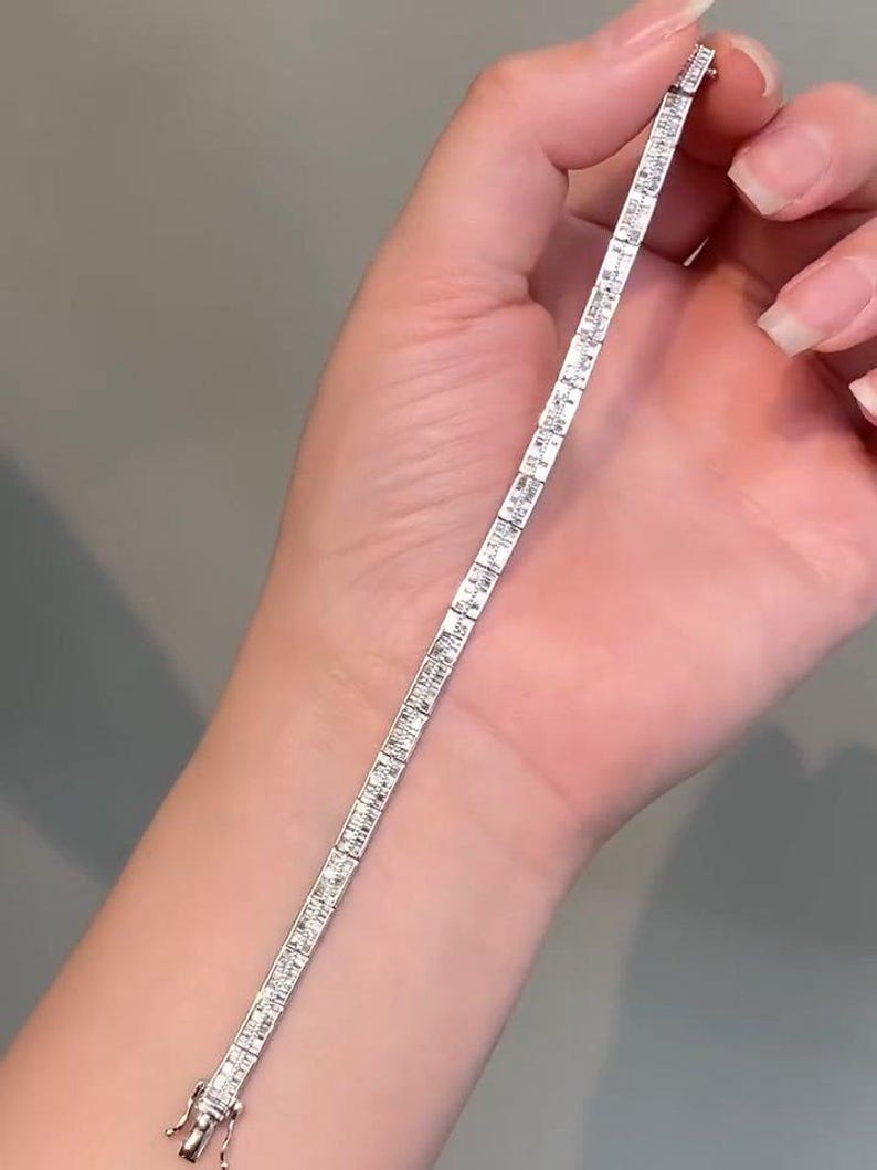 Pu&ograve; includere: Un bracciale tennis color argento caratterizzato da una fila continua di pietre trasparenti rettangolari taglio baguette incastonate in una montatura metallica. Il bracciale include una chiusura a cassetta sicura su un'estremit&agrave;.