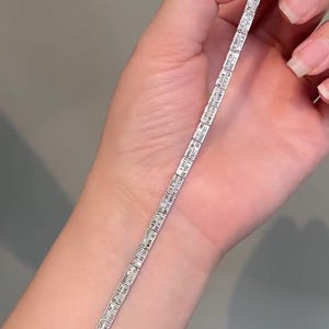 Pu&ograve; includere: Un bracciale tennis color argento caratterizzato da una fila continua di pietre rettangolari taglio baguette incastonate in una montatura metallica. Il bracciale presenta una chiusura a cassetta sicura a un'estremit&agrave; e maglie flessibili.