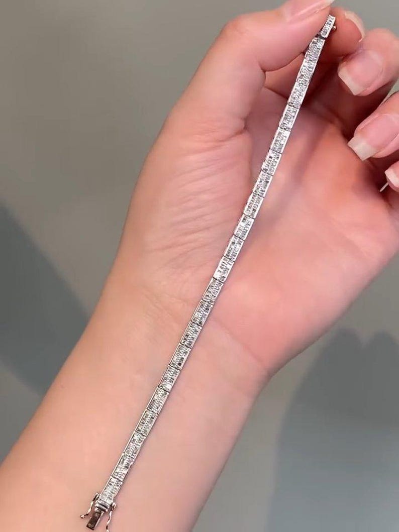 Pu&ograve; includere: Un bracciale tennis color argento caratterizzato da una fila continua di pietre rettangolari taglio baguette incastonate in una montatura metallica. Il bracciale presenta una chiusura a cassetta sicura a un'estremit&agrave; e maglie flessibili.