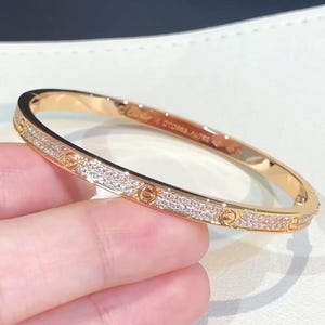 May include: A rose gold bangle bracelet featuring a pavé diamond-encrusted band with iconic screw motifs. The interior of the bracelet is engraved with the Cartier brand name, the serial number DTD883, and the Au750 gold purity hallmark.