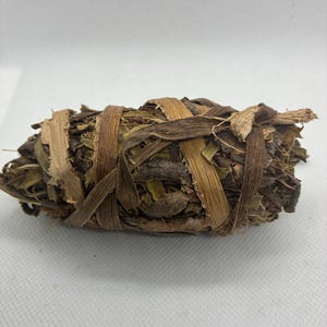 Puede incluir: Un manojo de hierbas secas, bien envuelto con tiras de fibra natural. Las hierbas son una mezcla de marrón, beige y verde, con un aspecto texturizado. El envoltorio es de color marrón claro. El fondo es blanco.