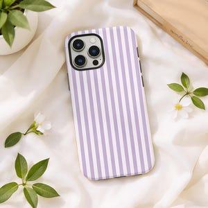 May include: A smartphone case with a vertical striped pattern in lavender and white. The case has a black border and a camera cutout. The case is lying on a white fabric with small white flowers and green leaves.