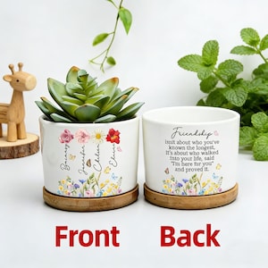 May include: Two white ceramic planters with a succulent plant. One planter has names and floral designs, the other has the text "Friendship" and a quote. Both sit on wooden saucers.