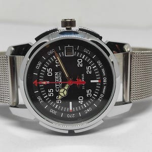 May include: A Citizen automatic wristwatch with a black dial, silver-tone case, and a mesh band. The watch face features white and red markings, including the text "CITIZEN AUTOMATIC". The watch has a date display at the 3 o'clock position.