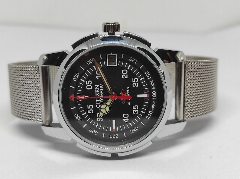 May include: A Citizen automatic wristwatch with a black dial, silver-tone case, and a mesh band. The watch face features white and red markings, including the text "CITIZEN AUTOMATIC". The watch has a date display at the 3 o'clock position.