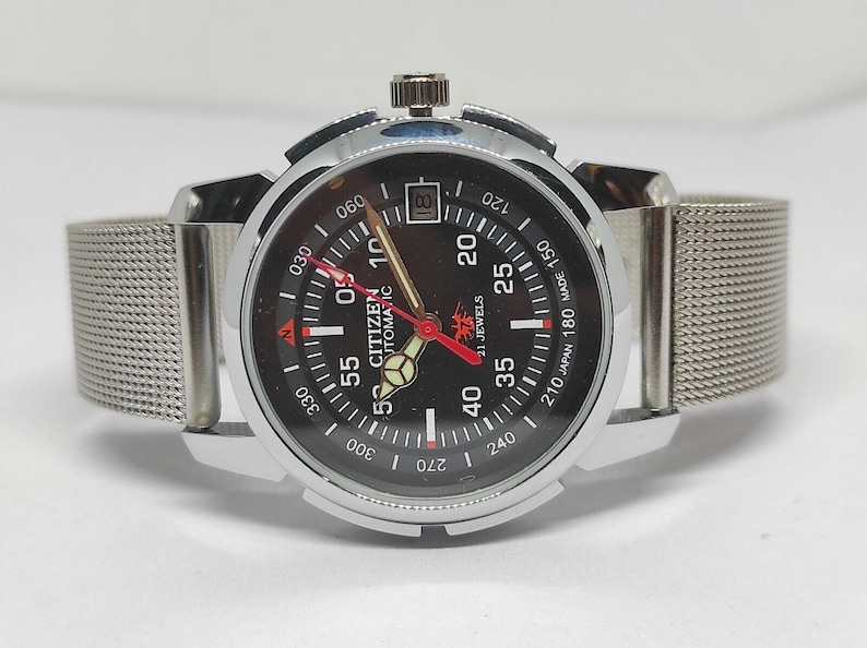 May include: A Citizen automatic wristwatch with a black dial, silver-tone case, and mesh band. The watch face features white and red markings, including the text "Citizen Automatic 21 Jewels". The watch has a date display at the 3 o'clock position.