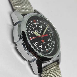 May include: A silver-toned Citizen automatic wristwatch with a black dial. The watch features red and white hands, a mesh band, and the text "CITIZEN AUTOMATIC" and "21 JEWELS".