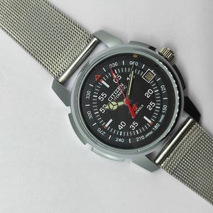 May include: A Citizen automatic wristwatch with a black dial, silver-tone case, and a mesh metal band. The watch face features white and red markings, including the text "CITIZEN AUTOMATIC". The watch has a date display at the 3 o'clock position.