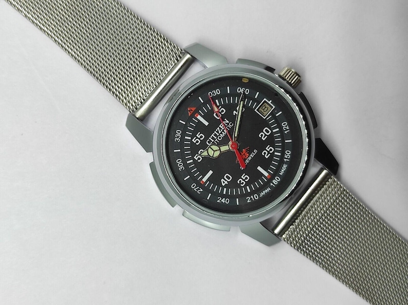 May include: A Citizen automatic wristwatch with a black dial, silver-tone case, and a mesh metal band. The watch face features white and red markings, including the text "CITIZEN AUTOMATIC". The watch has a date display at the 3 o'clock position.