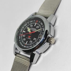 May include: A Citizen automatic wristwatch with a black dial, silver-tone case, and a mesh band. The watch face displays the time, date, and the text "CITIZEN AUTOMATIC". The watch has a silver crown and a rotating bezel.