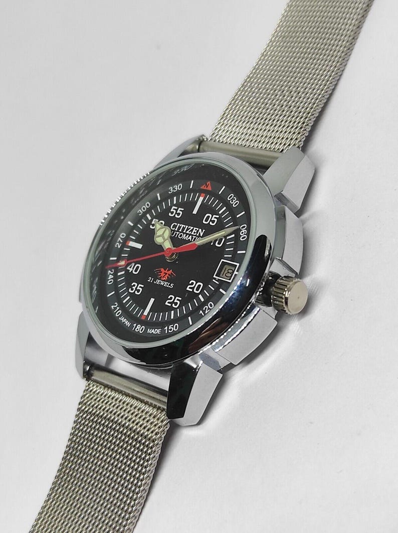 May include: A Citizen automatic wristwatch with a black dial, silver-tone case, and a mesh band. The watch face displays the time, date, and the text "CITIZEN AUTOMATIC". The watch has a silver crown and a rotating bezel.