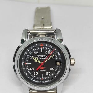 May include: A Citizen automatic wristwatch with a black dial, silver-tone case, and a silver mesh band. The watch face displays white numerals, red and white hands, and the text "Citizen Automatic 21 Jewels". The watch has a date window.
