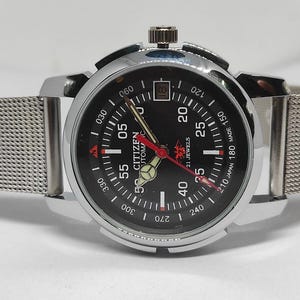 May include: A silver-toned Citizen automatic watch with a black dial, featuring white and red markings. The watch has a mesh band and a date display at the 3 o'clock position. The watch face displays the text "CITIZEN AUTOMATIC 21 JEWELS MADE IN JAPAN".