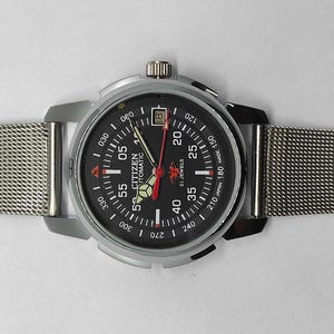 May include: A Citizen Automatic watch with a black dial, silver case, and mesh band. The watch face features white and red markings, including the date, and the hands are red and silver. The watch is a classic timepiece.