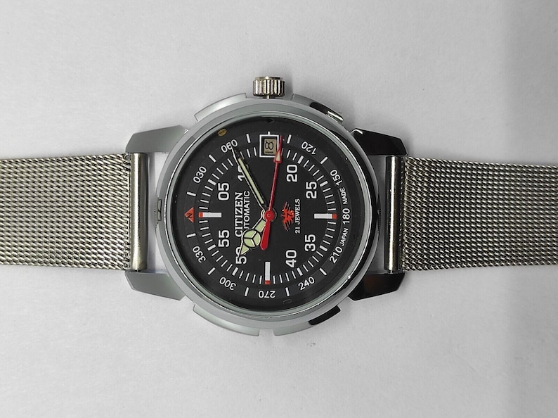 May include: A Citizen Automatic watch with a black dial, silver case, and mesh band. The watch face features white and red markings, including the date, and the hands are red and silver. The watch is a classic timepiece.