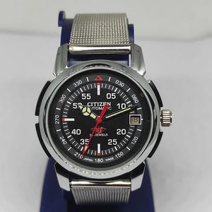 May include: A Citizen automatic wristwatch with a black face, silver-tone case, and a mesh band. The watch features a date window and luminous hands. The dial includes the text "Citizen Automatic" and "Japan Made".