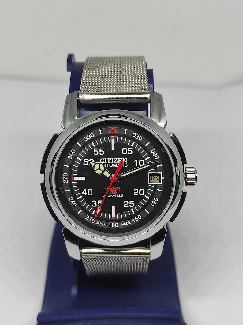 May include: A Citizen automatic wristwatch with a black face, silver-tone case, and a mesh band. The watch features a date window and luminous hands. The dial includes the text "Citizen Automatic" and "Japan Made".