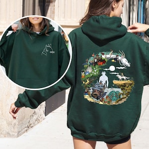 May include: Dark green hoodie featuring a white graphic of a cartoon character on the front and a colorful illustration on the back. The hoodie has a kangaroo pocket and a drawstring hood. The back graphic depicts a fantasy scene.