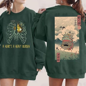 May include: Dark green sweatshirt. The front features a rib cage graphic with a yellow heart and the text "A HEART'S A HEAVY BURDEN." The back has a Japanese-style illustration of a moving castle.