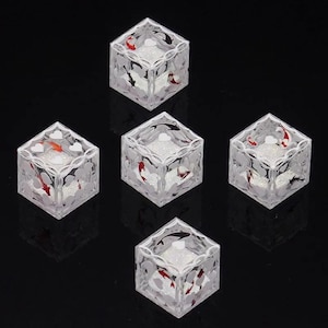 May include: Five clear, transparent cubic blocks featuring internal designs of red, white, and black koi fish swimming among white heart shapes. Each cube has a textured, glittery white base and a decorative white lattice pattern on the top edges.