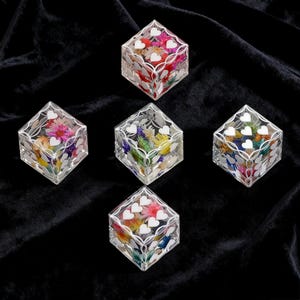 May include: Five clear resin cubes arranged in a pentagon formation. Each cube contains colorful dried flowers embedded inside and features white heart-shaped decals applied to the exterior surfaces, creating a decorative floral display.