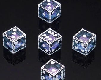 Puede incluir: Un conjunto de cinco dados azules translúcidos con interiores morados brillantes. Cada dado presenta puntos blancos en forma de corazón en las caras y un patrón de borde blanco estilo filigrana a lo largo de los bordes de estas piezas.
