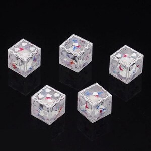 May include: Five clear, cube-shaped dice featuring white heart icons on each face. The interior of each die contains a glittery, textured substance with visible red and blue accents, while the edges are outlined with a white, decorative filigree pattern.
