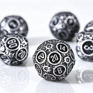 May include: A set of spherical polyhedral dice with a dark, weathered metallic finish. Each die features recessed circular frames containing white numerals, including a prominent 20 on the front-most die, with a textured, distressed surface.