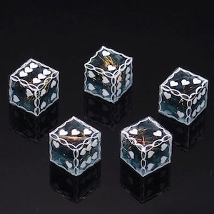 May include: A set of five translucent blue dice with white heart-shaped pips and white chain-link borders. Each die contains embedded iridescent gold-toned metallic fibers visible through the clear resin material, creating a reflective effect.
