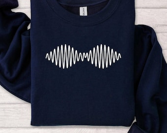 May include: Navy blue sweatshirt featuring a white graphic design. The design is a series of vertical lines arranged in a wave-like pattern. The sweatshirt has a crew neck and long sleeves.