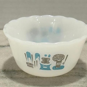 Puede incluir: Un cuenco blanco con borde festoneado y un diseño gráfico azul y gris. El cuenco presenta una serie de imágenes estilizadas, incluyendo herramientas y un árbol. El cuenco está hecho de un material blanco lechoso.
