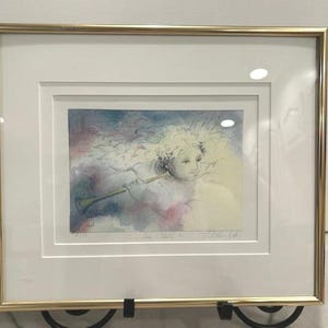 May include: Framed art print featuring a watercolor illustration of an angel playing a trumpet. The artwork has soft pastel colors, including blues, pinks, and yellows. The print is set in a white mat and a gold-colored frame, creating an elegant presentation.