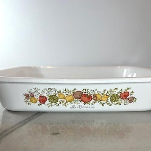 May include: White rectangular baking dish with a colorful border of illustrated vegetables and the text "Le Romarin". The border features tomatoes, lemons, artichokes, and other produce. The dish is made of a durable material.