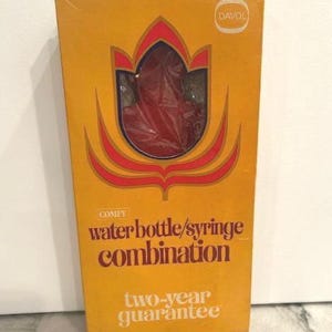 May include: A vintage box with a retro design, featuring the text "COMFY water bottle/syringe combination." The box is yellow with a red and orange floral design and the text "two-year guarantee."