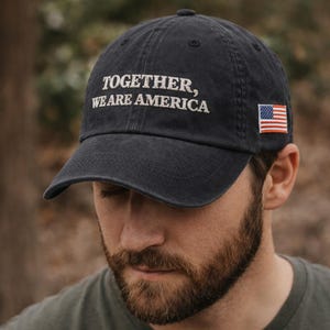 Może przedstawiać: Czarna czapka bejsbolowa z białym haftem "TOGETHER, WE ARE AMERICA". Czapka posiada małą naszywkę z flagą amerykańską. Kapelusz wykonany jest z miękkiego, zużytego materiału.
