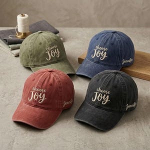 以下が含まれることがあります： 緑、青、赤、黒の4色の野球帽。各キャップには、前面に「choose JOY」の刺繍、側面に「Jennifer」の名前があります。キャップは、使い古された質感のある生地で作られています。