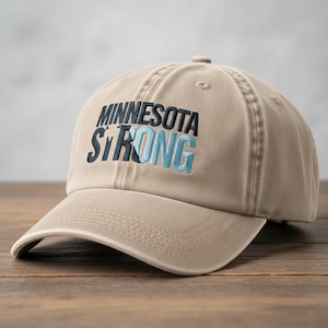 以下が含まれることがあります： 濃い青と水色の「MINNESOTA STRONG」の刺繍が施された、ベージュ色の野球帽。帽子はカーブしたつばと布製のストラップ留めが付いています。丈夫な素材で作られています。