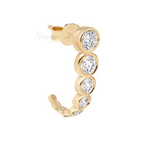 May include: A gold-colored earring with a curved design. The earring features a series of round, bezel-set, clear gemstones. The earring curves from the post, with the gemstones decreasing in size. The earring is set against a white background.