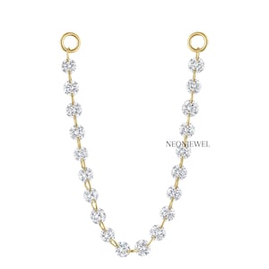 Puede incluir: Una delicada cadena de oro con brillantes gemas redondas y transparentes. La cadena conecta dos pequeños bucles de oro, con el texto "NEONJEWEL" en el centro. La joya está sobre un fondo blanco.
