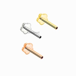 May include: Three metal nose studs in silver, gold, and rose gold. Each stud features a four-leaf clover design on the top and a straight post. The studs are displayed against a white background.