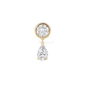 May include: A gold earring featuring a round brilliant-cut clear stone in a bezel setting, connected by a small link to a dangling pear-shaped clear stone in a prong setting. The piece has a polished gold finish and a clear, faceted appearance.