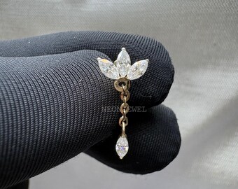 May include: A gold-toned earring featuring a floral design with three marquise-cut white gemstones at the top, connected by a chain to a single dangling gemstone. The earring is set against a dark background.