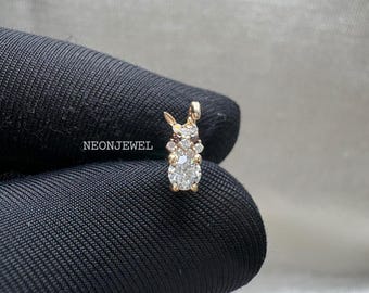 May include: A gold bunny pendant, adorned with clear and brown gemstones. The bunny features a large, round, clear gemstone at its base. The pendant is displayed on a black surface. The text "NEONJEWEL" is visible.
