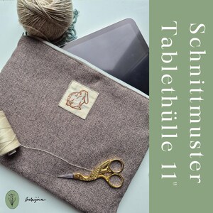 May include: A brown tablet sleeve with a herringbone pattern, a white zipper, and a small patch with a rabbit illustration. The text "Schnittmuster Tablethülle 11" is visible. A tablet is partially visible inside the sleeve.