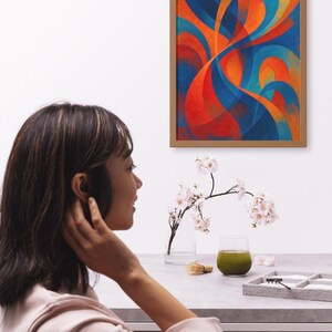 May include: An abstract painting in a wooden frame, featuring flowing shapes in shades of blue, orange, and red. A woman is seen in the foreground, with a table set with a glass of green liquid, a small brush, and a tray.