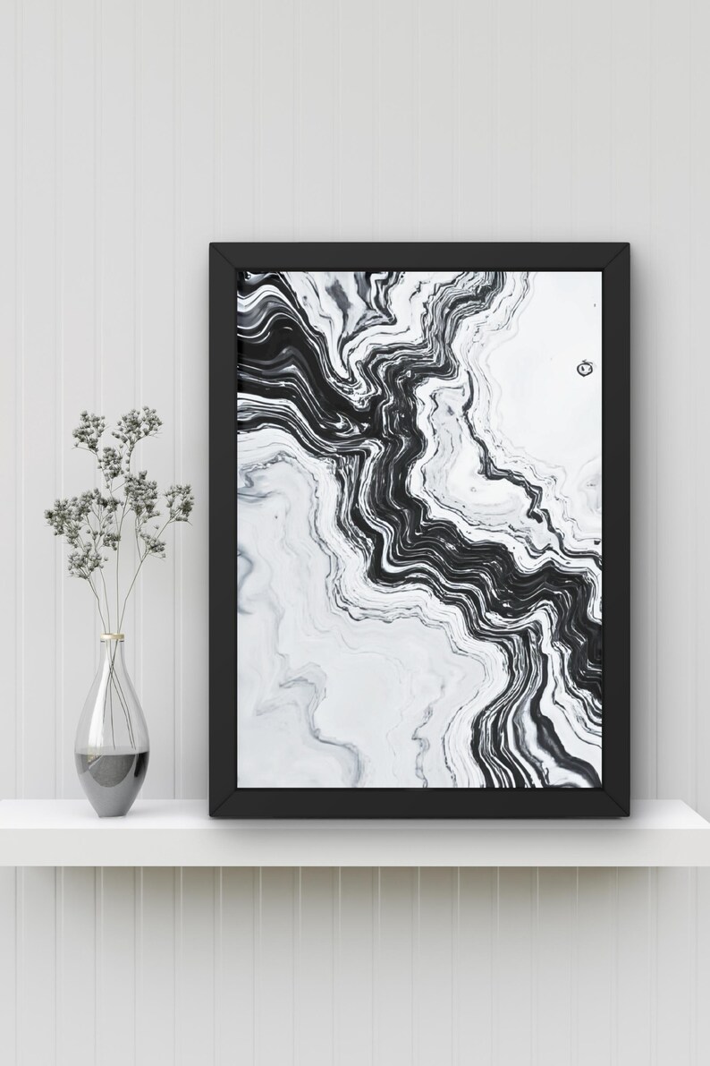 May include: Black and white abstract art print in a black frame. The artwork features a flowing, marbled design. A clear glass vase with dried flowers sits on a white shelf below the framed art.