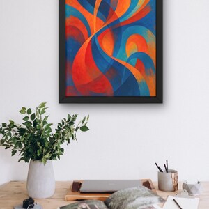 May include: Abstract art print in a black frame. The artwork features flowing, curved shapes in shades of blue, orange, and red. The framed art is displayed above a wooden desk with a vase of greenery, a laptop, and an open book.
